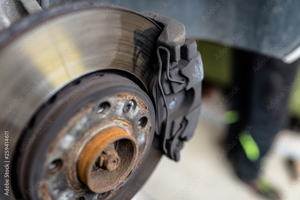 Front brake discs with caliper and brake pads in the car, on a car lift in a workshop. Front brake discs with caliper and brake pads in the car, on a car lift in a workshop.