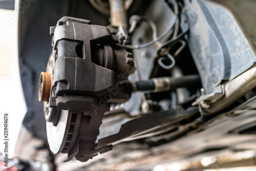 Front brake discs with caliper and brake pads in the car, on a car lift in a workshop.