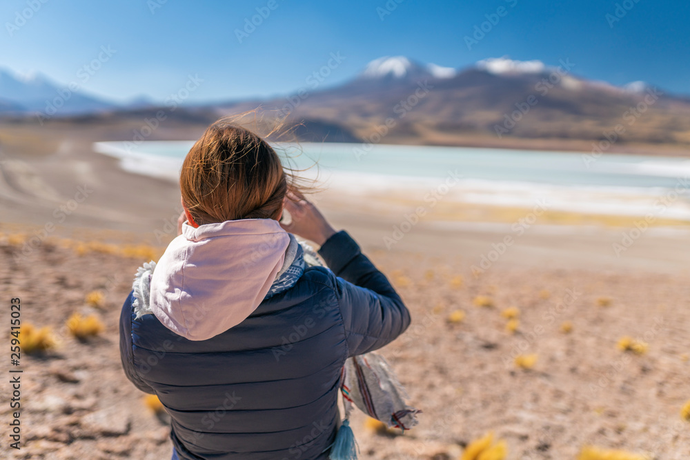 Landscape woman photographer taking mobile phone photos in an amazing wilderness environment at Atacama Desert Andes mountains lagoons. A woman cut out silhouette over the awe Tuyajto Lagoon scenery
