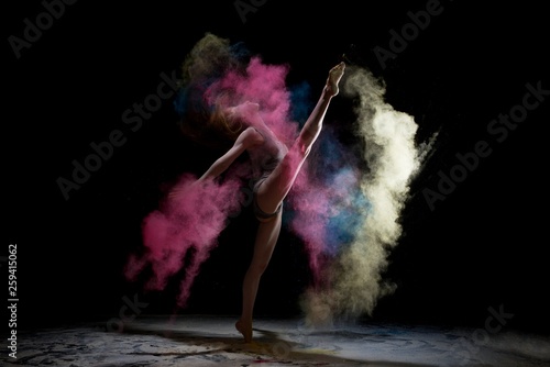 Slim woman jumping in color dust cloud in the dark