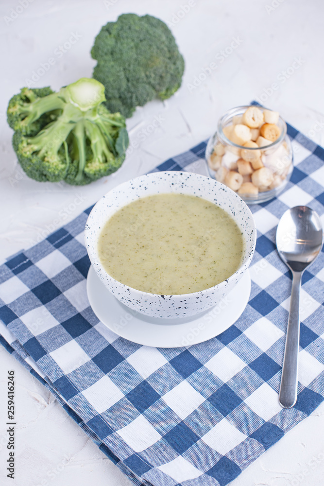 Cream soup puree with broccoli, cream and crackers. Lunch of vegetables on a light background. Plate and napkin on the table Cream soup puree with broccoli, cream and crackers. Lunch of vegetables on a light background. Plate and napkin on the table