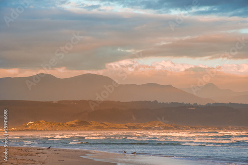 Rays of golden evening light falling on the Plettenberg Bay beach at sunset, with mountains in the distance. Garden Route, Western Cape, South Africa