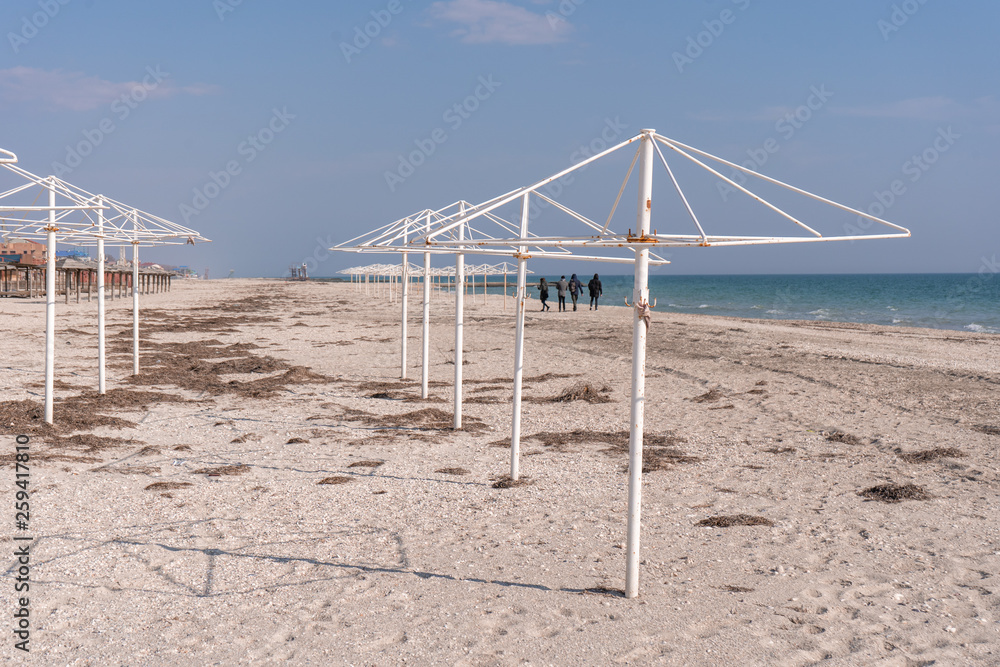 People walking along the sea beach behind the rusty umbrella supports