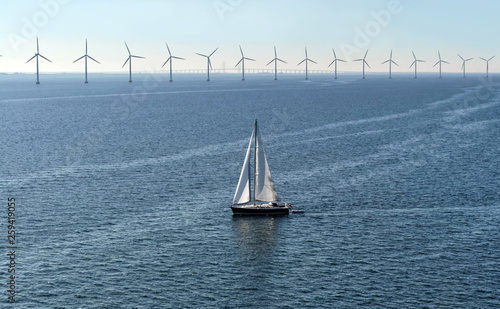 A yacht with a white sail in the sea on the background of wind turbines, in the background a bridge connecting Denmark and Sweden