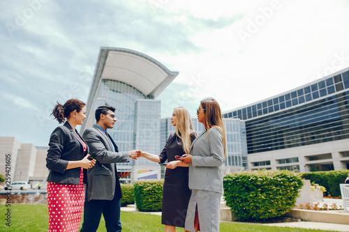 Handsome businessman in a city. Businessman in a glasses. Business partners in a summer city. Man and three women standingin a sity with tablet and phones photo