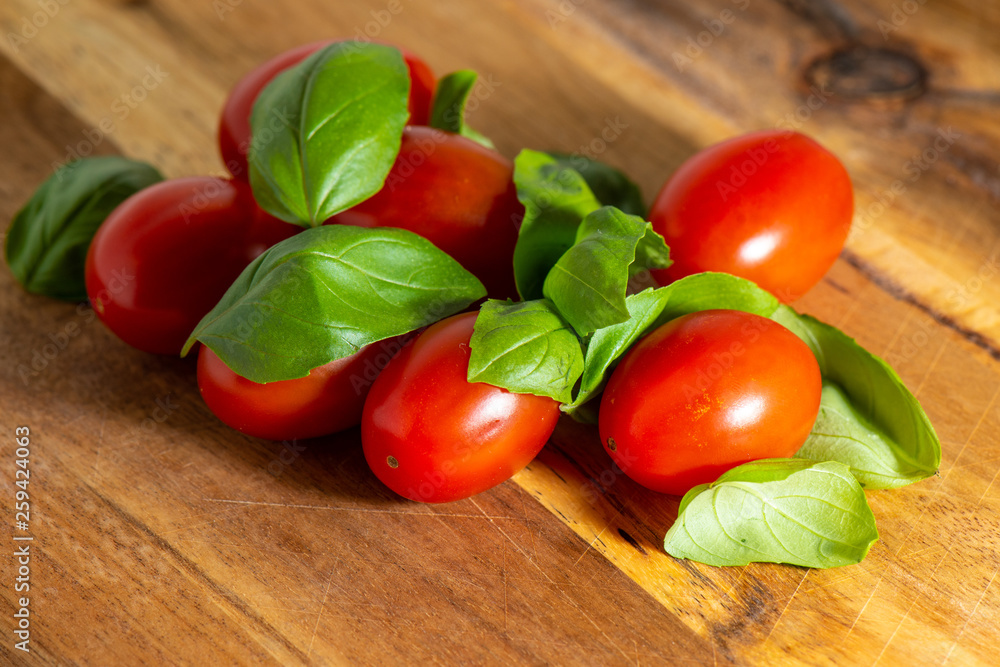 Red tomato on a cutting board with basil leaves on wooden background.. Red tomato on a cutting board with basil leaves on wooden background..
