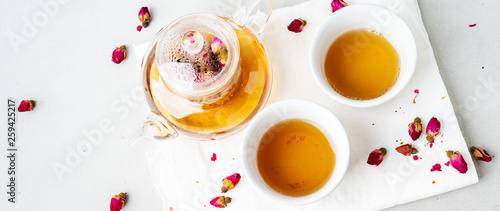 Herbal tea with dried pink flower roses buds in transparent teapot over gray background, top view, copy space. Long wide banner.