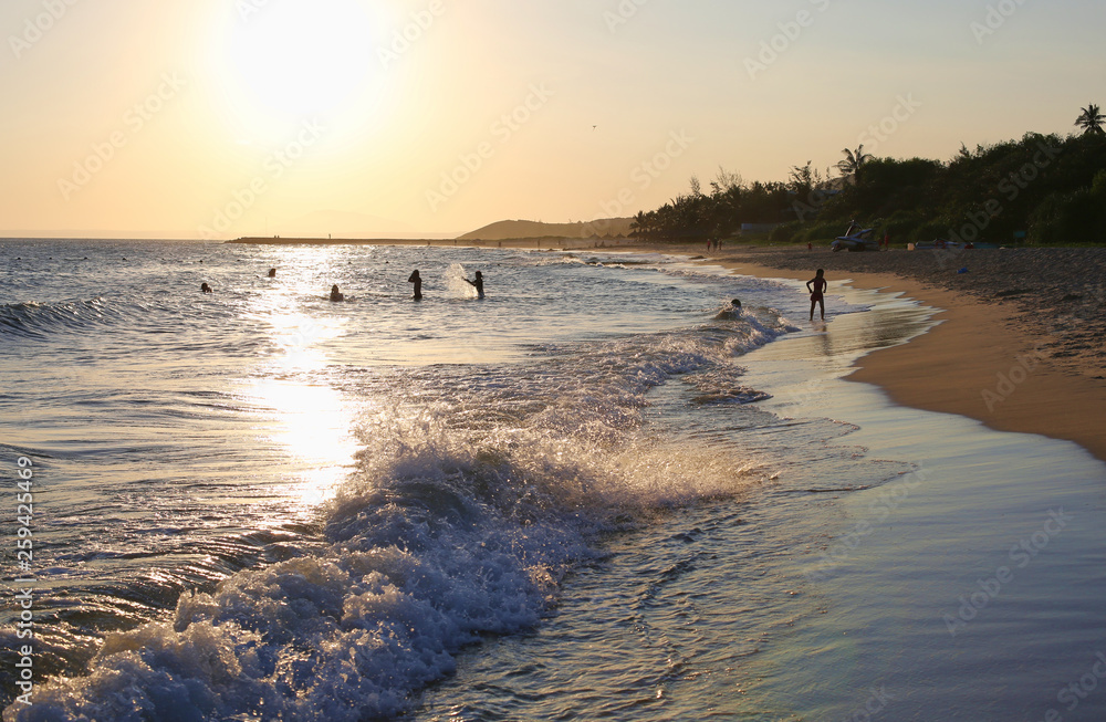 Happy people swimming in sunset rays. Vietnam beach. Family vacations idea. Ocean waves hitting coastline. Sandy beach. 