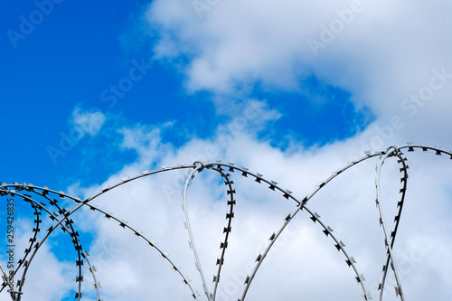 Barbed wire fence with blue sky and white clouds.