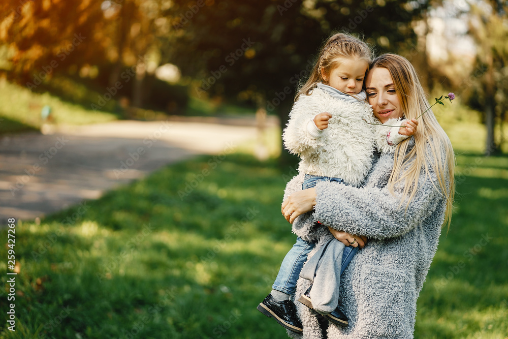 young blonde mother holding her toddler daughter in her arms as they are walking through the park on a sunny day young blonde mother holding her toddler daughter in her arms as they are walking through the park on a sunny day