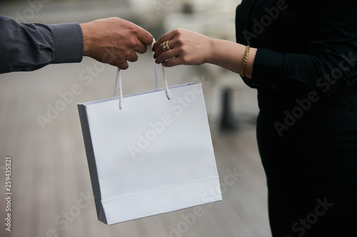 Man giving gift in paper bag to woman, close-up