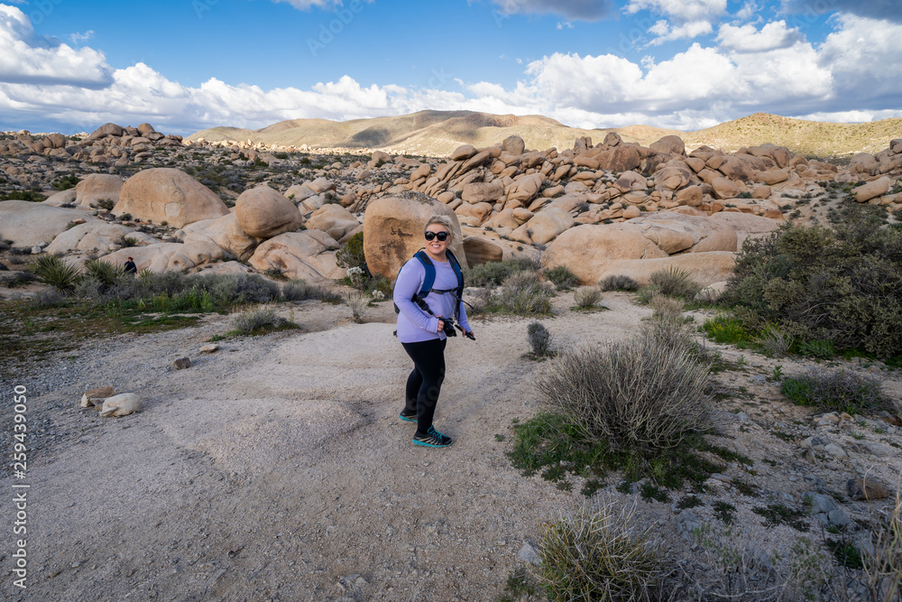 Young woman female hiker wearing a backpack starts off on a hiking trail in Joshua Tree National Park, to the Arch Rock