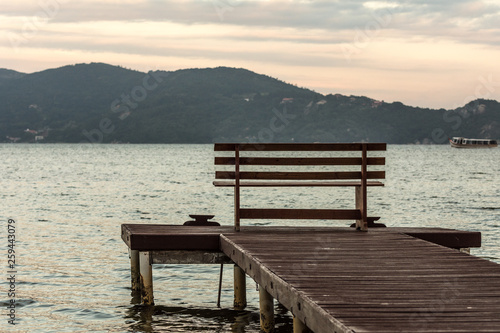 Wooden bench on a pier in front of the Conceicao Lagoon during a sunny day, in Florianopolis, Brazil.
