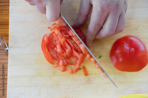 cooking, food and home concept - close up of male hand cutting tomato on cutting board at home