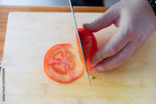 cooking, food and home concept - close up of male hand cutting tomato on cutting board at home photo