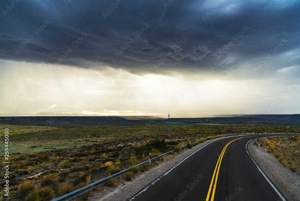 Highway road against the background of rain dark clouds, steppes, and mountains in Patagonia, Argentina