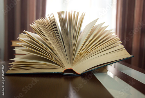 thick open book in fan on wooden table against backlight