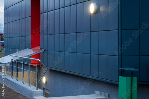 Descent to the basement. Stair down. New building. Beautiful stylish tiled red-blue facade. Lamp and green trashcan.