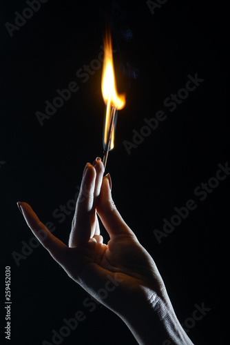 elegant female hand holding burning match on dark background  