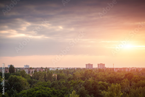 Abandoned uninhabited city overgrown with trees and bushes. Dark region of the radioactive town in the evening. Houses in the woods at sunset.