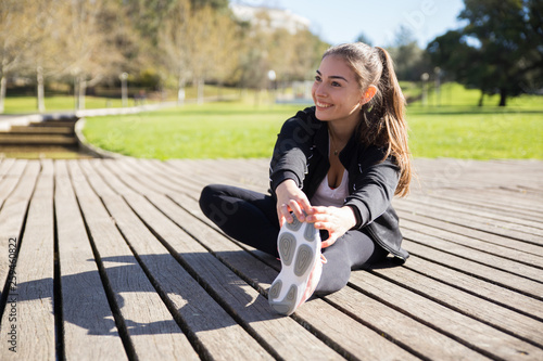 Smiling young lady stretching leg outdoors photo