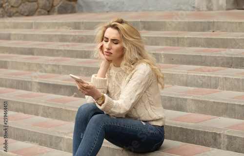 Blonde woman sitting on stairs with phone in the city.