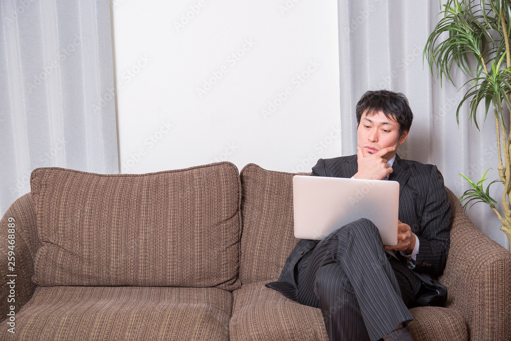 ソファでPCを開く男性 ソファでPCを開く男性