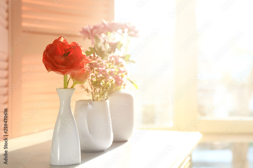 Vases with beautiful flowers on table in room Vases with beautiful flowers on table in room