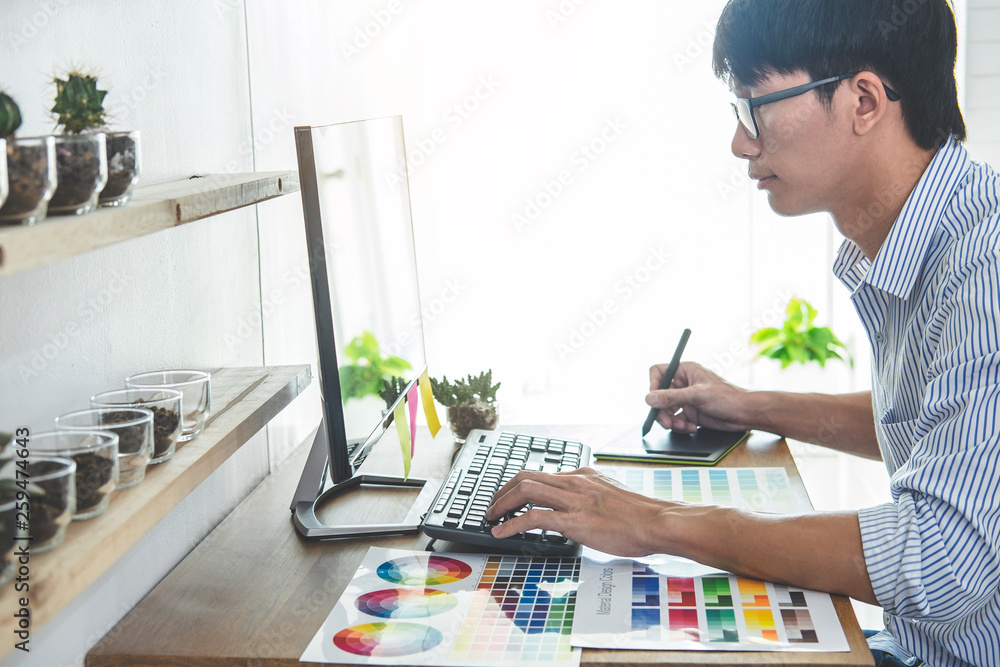 Image of male creative graphic designer working on color selection and drawing on graphics tablet at workplace with work tools and accessories in workspace Image of male creative graphic designer working on color selection and drawing on graphics tablet at workplace with work tools and accessories in workspace