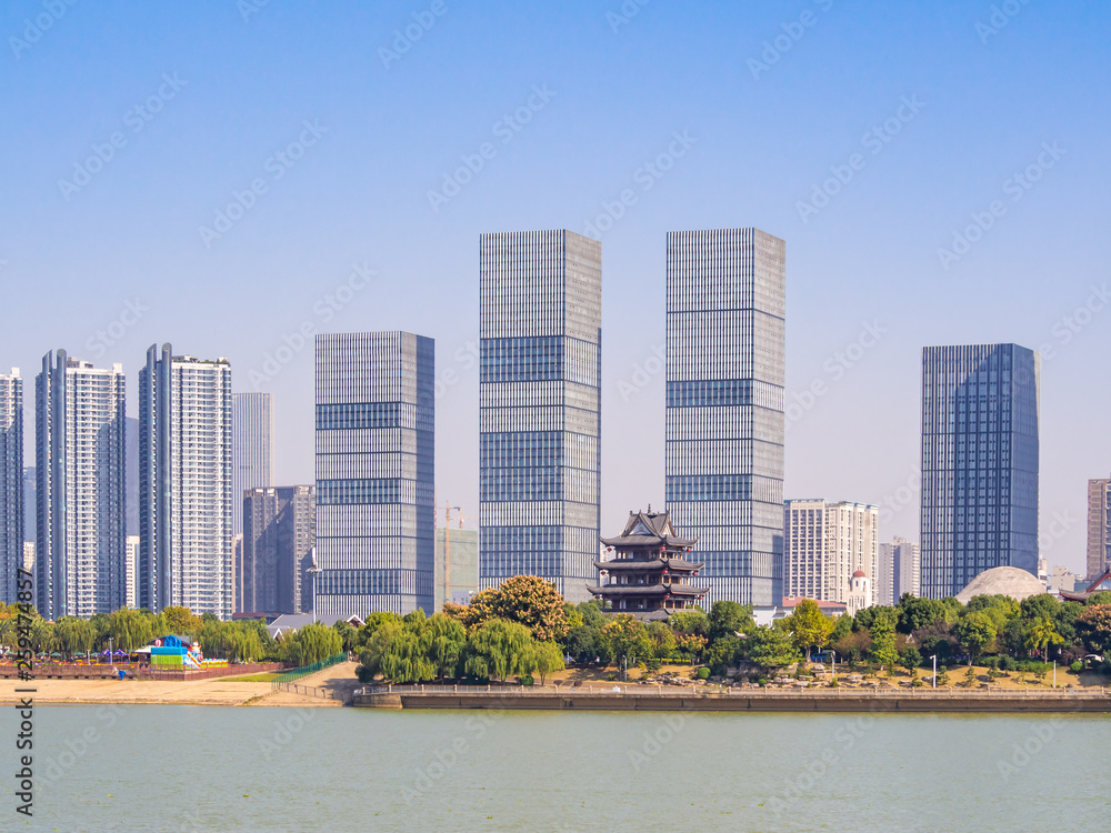 View at the bank of Xiang river in Changsha, the main city of Hunan Province, China. There are tall modern buildings, as well as traditional pavillion standing beside. Asian cityscape on a sunny day.