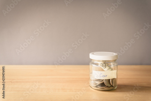 Coin in a glass jar on wooden desk with copy space, Saving money for buy a car concept
