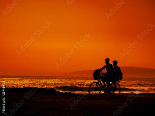 Two friends are riding bicycle at sunset