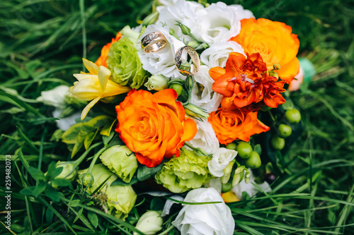 Beautiful wedding bouquet is lying in the grass. Engagement rings are on the flowers. Orange colours of fall and autumn in floral composition.