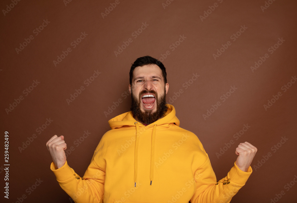 Happy young man celebrating his success over yellow background 