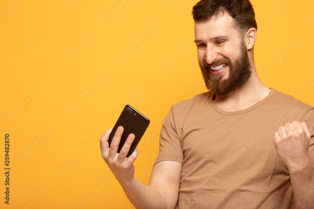 Portrait of an excited man standing over yellow background, holding mobile phone, celebrating Portrait of an excited man standing over yellow background, holding mobile phone, celebrating