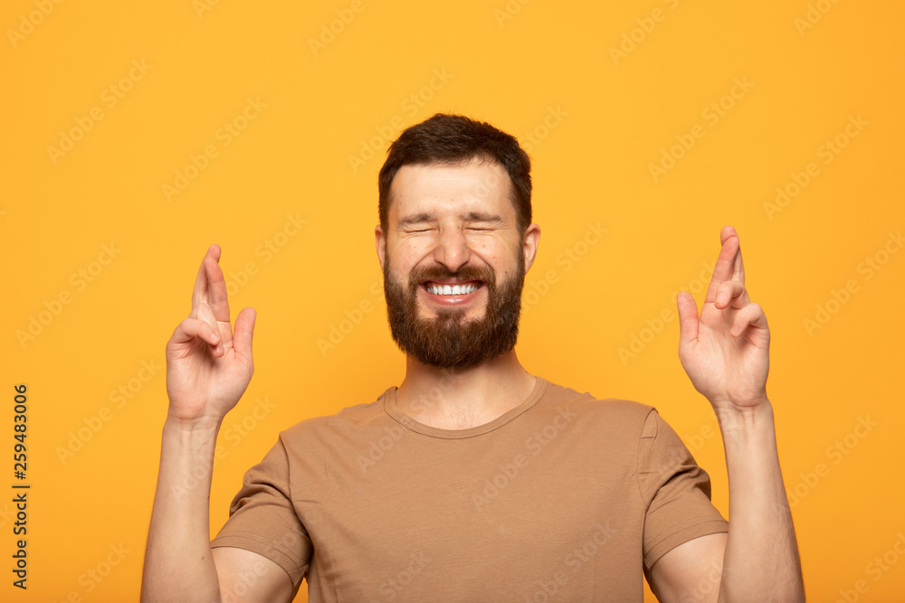 Glad positive bearded man crosses fingers, closes eyes with pleasure, anticipate hearing good news, isolated color background. Happy male rejoices that his dreams came true. Excitement concept Glad positive bearded man crosses fingers, closes eyes with pleasure, anticipate hearing good news, isolated color background. Happy male rejoices that his dreams came true. Excitement concept