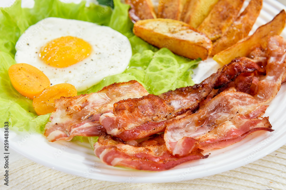 Fried bacon with French fries and a delicate egg, close-up. Fried bacon with French fries and a delicate egg, close-up.