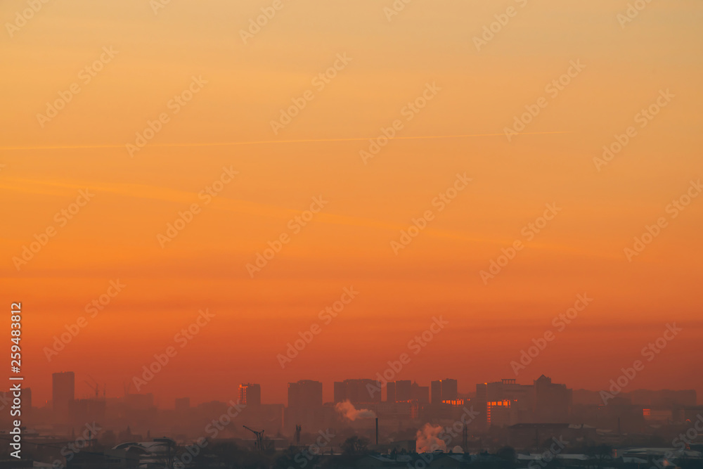 Urban high-rise buildings behind private houses on sunset. Silhouettes of big city buildings. Warm backlight of dawn. Private sector near apartment houses in sunlight. Minimalist cityscape at sunrise.