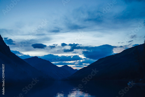 Amazing blue silhouettes of mountains on dusk. Dawn sky reflected in mountain lake. Wonderful atmospheric highland landscape. Beautiful ripples on lake water with twilight bright. Scenic mountainscape