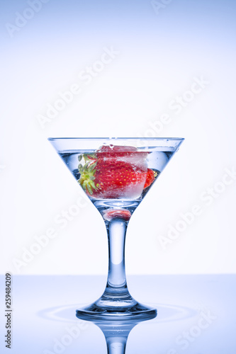 Strawberries in a glass with ice. Strawberry Cocktail. Frozen splashes of clean, spring water, in a glass with frozen strawberries, on a white background.