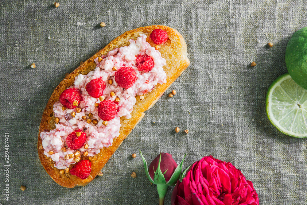 wholegrain toast with honey cottage cheese and raspberry on the table covered with a canvas with a lime and flowers of a rose