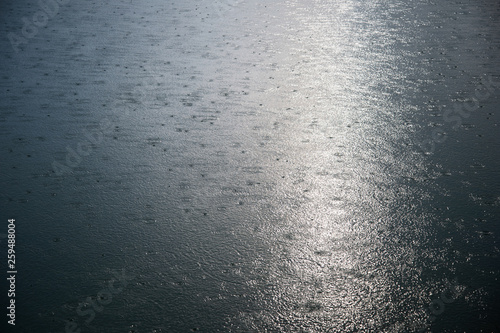 ripple drop of rain on water surface of the sea or lake with silver glowing of sunlight nature textured background