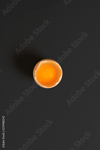 Single egg broken yolk view top. Black background text copy space.