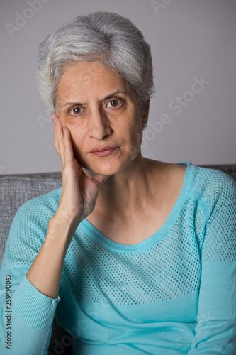 Portrait of senior woman thinking sitting on sofa with hand on chin 