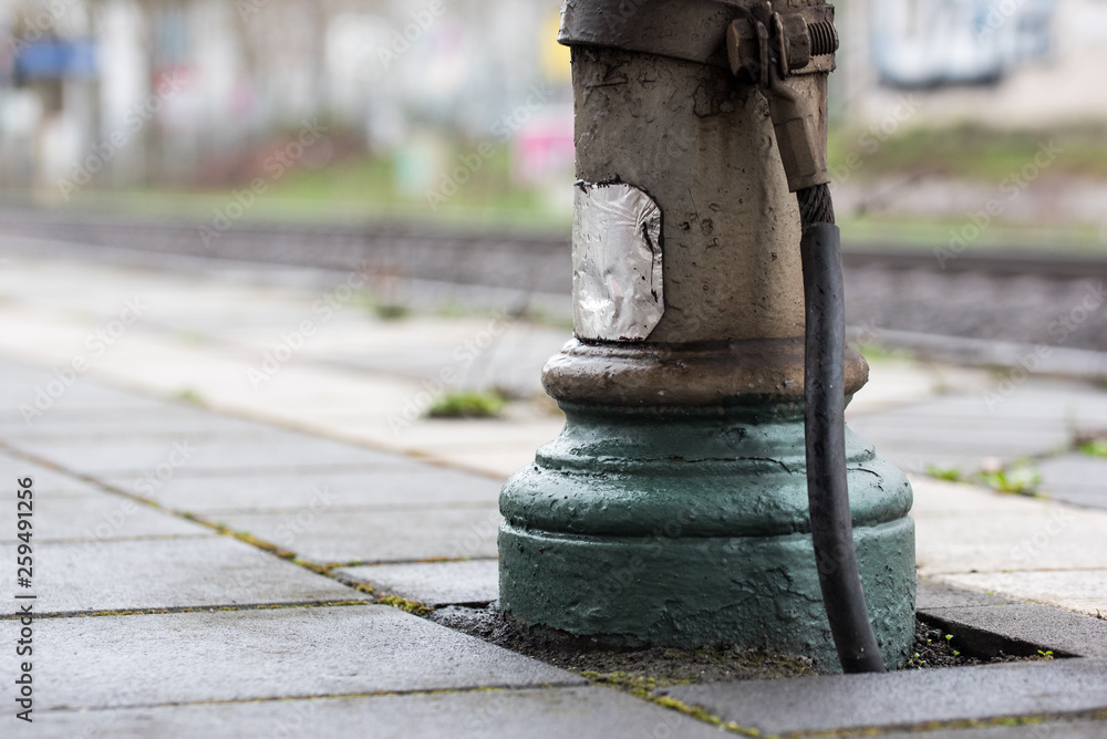 old metallic post with a big cable or wire and green and grey painting standing at a railwaystation and blurred background old metallic post with a big cable or wire and green and grey painting standing at a railwaystation and blurred background