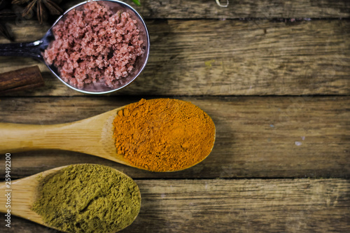 Close up of turmeric powder in wooden spoon with other blurred spices and asian ingredients on wooden deck.