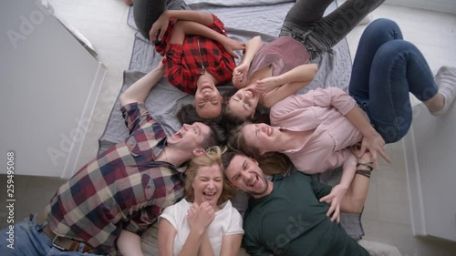 friends tickle each other while lying on their backs and laughing merrily at the camera during a home party
