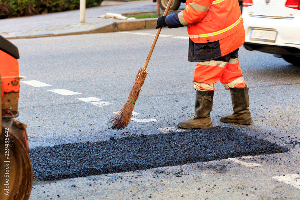 A road builder collects fresh asphalt on part of the road and levels it for repair in road construction.