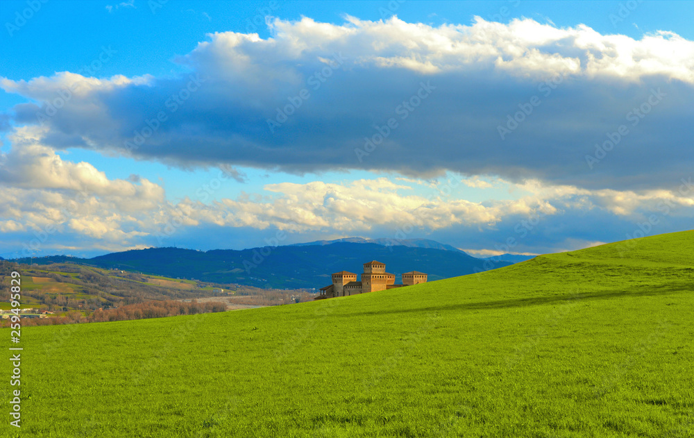 green landscape on hills around Parma and grass field near Torrechiara castle and cloudy blue sky in background,  Italy