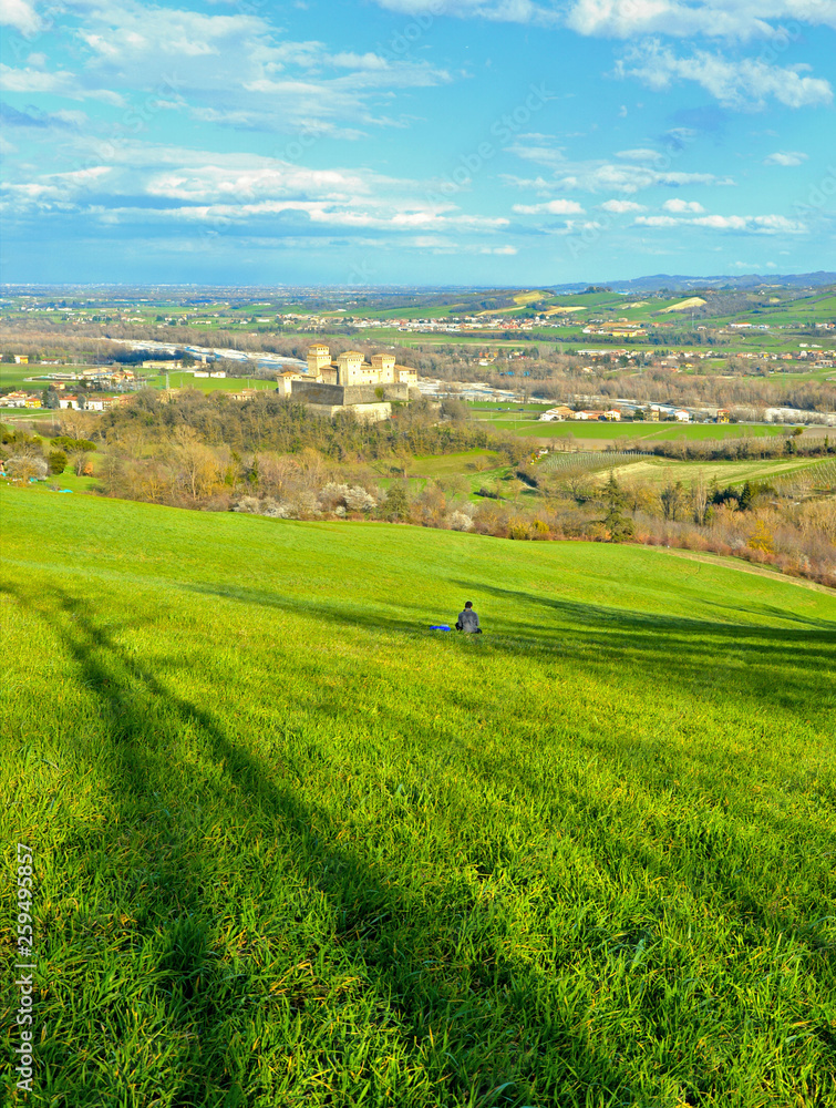 green landscape on hills around Parma with lonely person sitting in grass field near Torrechiara castle and watching panorama,  Italy